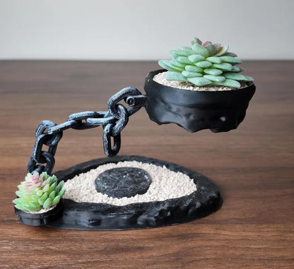 Vaso scultoreo con catena metallica e pianta succulenta su tavolo